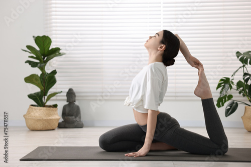 GIrl practicing one legged king pigeon asana on mat in yoga studio. Eka pada rajakapotasana pose photo