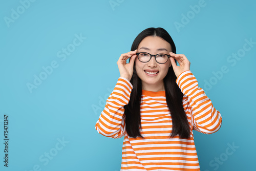 Portrait of happy woman in glasses on light blue background. Space for text