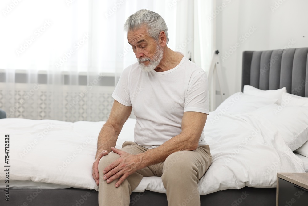 © New Africa - Arthritis symptoms. Man suffering from pain in knee on bed at home