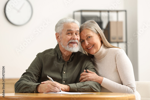 Happy senior couple signing Last Will and Testament indoors photo