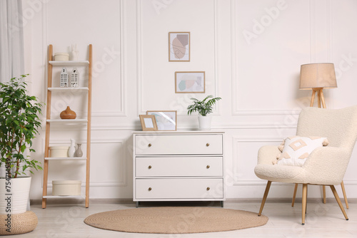 Picture frames hanging on white wall  chest of drawers and armchair in living room