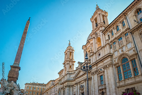 Sant'Agnese in Agone church and obelisk of Fontana dei Fiumi fountain on the Piazza Navona with bright sun shining from the bell tower, Rome, Italy.
