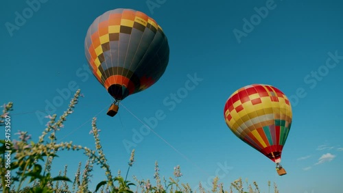 Two hot air balloons float over a tall grass field in the sky
