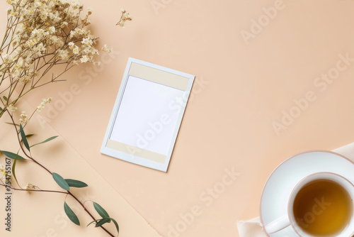 Flat lay, top view office desk workspace with blank photo frame, cup of tea and gypsophila flowers on pastel beige background.