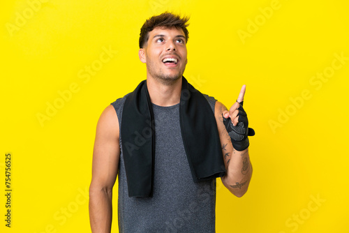 Young sport caucasian man with towel isolated on yellow background pointing up and surprised