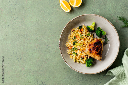 Bowl with chicken, pasta orzo with vegetables in Mediterranean style on a green background.