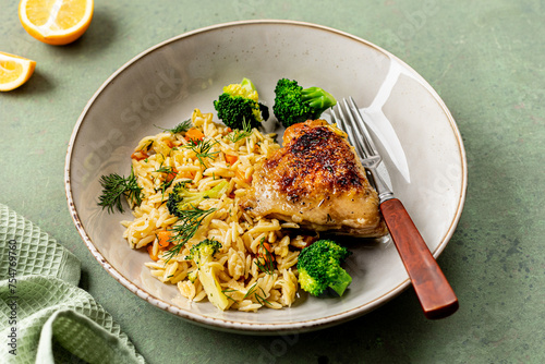 Bowl with chicken, orzo pasta with vegetables on a green background.