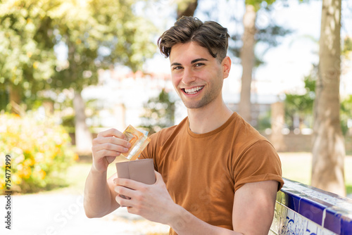 Young handsome man holding wallet with money with happy expression