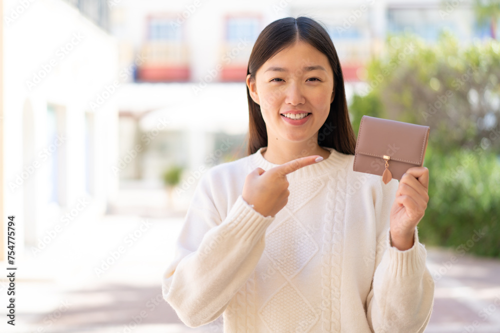 Pretty Chinese woman holding a wallet at outdoors and pointing it Pretty Chinese woman holding a wallet at outdoors and pointing it