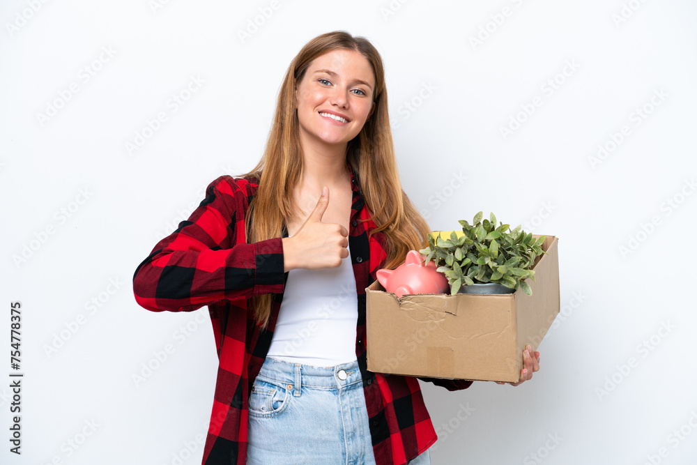 Young caucasian woman making a move while picking up a box full of things isolated on white background giving a thumbs up gesture Young caucasian woman making a move while picking up a box full of things isolated on white background giving a thumbs up gesture