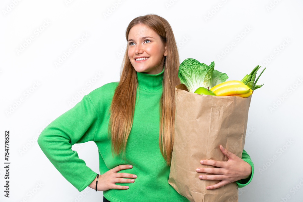 Young caucasian woman holding a grocery shopping bag isolated on white background posing with arms at hip and smiling Young caucasian woman holding a grocery shopping bag isolated on white background posing with arms at hip and smiling