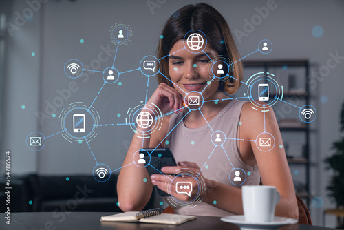 Smiling businesswoman in casual wear holding using smartphone typing at office workplace with notebook. Concept of distant work, business education. Social network icons chain hologram