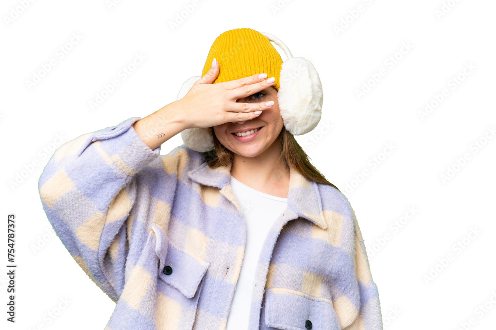 Young blonde woman wearing winter muffs over isolated chroma key background covering eyes by hands and smiling Young blonde woman wearing winter muffs over isolated chroma key background covering eyes by hands and smiling