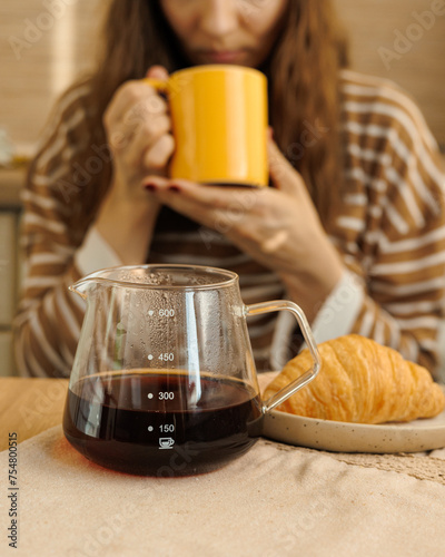 female makes coffee in morning kitchen. brews in purover. yellow cup with black coffee drip. daily routine of happy woman. Food and drinks, croissant on table. Americano cappuccino for cheerfulness photo
