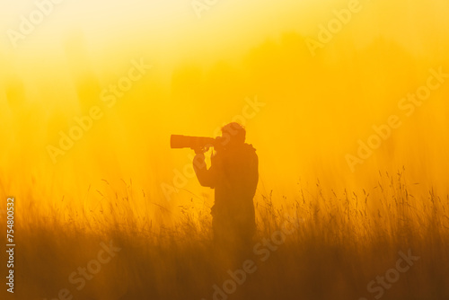 A man standing in a field with a camera, capturing the beauty of the sunset.
