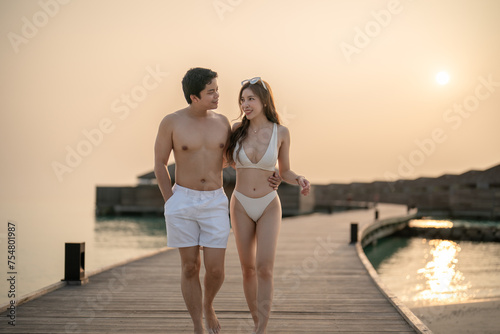 Couple walking on wooden bridge by the beach during sunset. photo