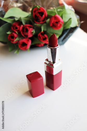 red lipstick and bouquet of flowers on white background