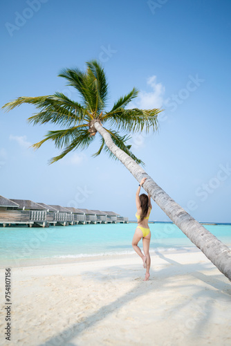 Woman in yellow bikini posing under the coconut trees on tropical beach.
