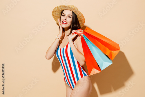 Side view young woman wear one-piece swimsuit hat hold shopping package bags isolated on plain blue cyan color background studio. Summer vacation sea rest sun tan, Black Friday sale buy day concept.