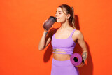 Young fitness trainer instructor sporty woman sportsman wear purple top clothes in home gym holding yoga mat drink protein cocktail isolated on plain orange background. Workout sport fit abs concept.