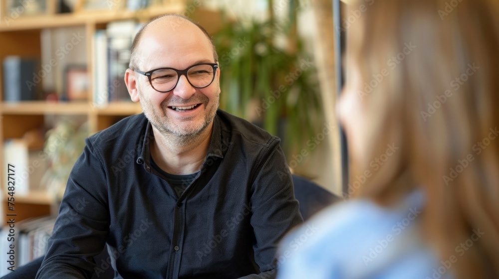 A joyful bald man in black engaging in a lighthearted conversation with a blurred person. A joyful bald man in black engaging in a lighthearted conversation with a blurred person.