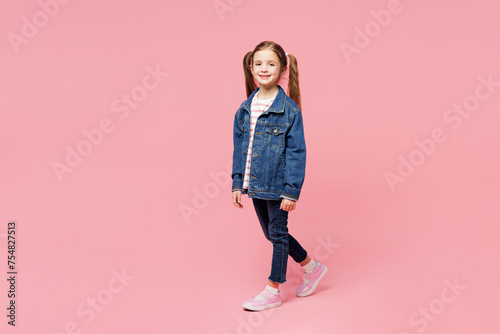 Full body side view little child cute kid girl 7-8 years old wears denim shirt have fun walk go look camera isolated on plain pastel light pink background. Mother's Day love family lifestyle concept.