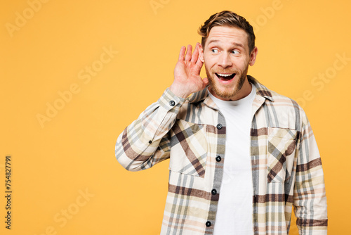 Young curious nosy smiling Caucasian man he wear brown shirt casual clothes try to hear you overhear listening intently isolated on plain yellow orange background studio portrait. Lifestyle concept. photo