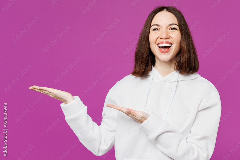 Young smiling fun happy Caucasian woman she wear light hoody casual clothes point hands arms aside indicate on area mockup isolated on plain purple color background studio portrait. Lifestyle concept.