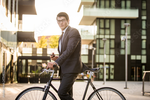 Fototapeta Naklejka Na Ścianę i Meble -  Handsome young business man wearing elegant corporate suit going to work with bicycle, concepts of transportation, green mobility and eco friendly lifestyle