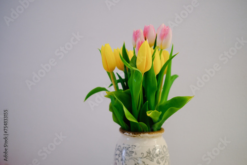 tulips in an old vintage vase against a white wall yellow and pink flowers in a vase on a table
