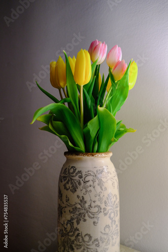 tulips in an old vintage vase against a white wall yellow and pink flowers in a vase on a table