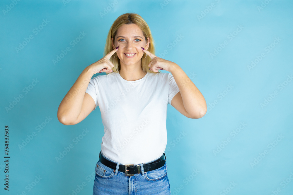 Young beautiful woman wearing casual t-shirt over isolated blue background smiling confident showing and pointing with fingers teeth and mouth Young beautiful woman wearing casual t-shirt over isolated blue background smiling confident showing and pointing with fingers teeth and mouth