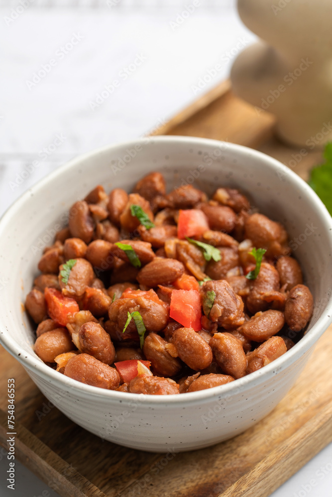 Food dish made of beans, tomatoes, and cilantro on a wooden table Food dish made of beans, tomatoes, and cilantro on a wooden table