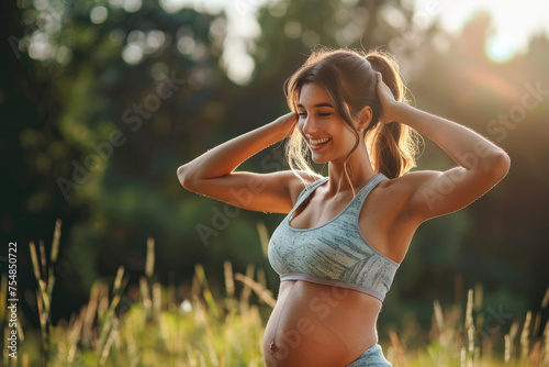 Beautiful smiling pregnant woman in sportswear showing muscles outdoors. Pregnancy and healthy lifestyle concept