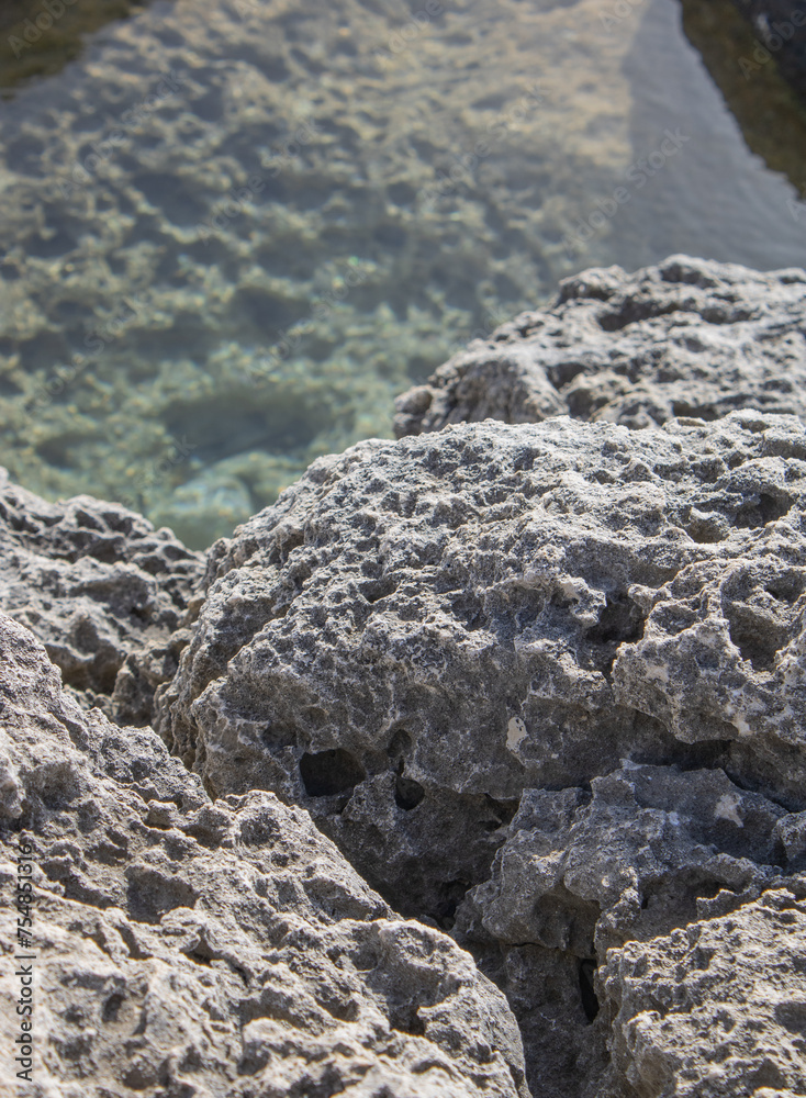 close-up of porous light-colored stone on a cliff, clear water in the background