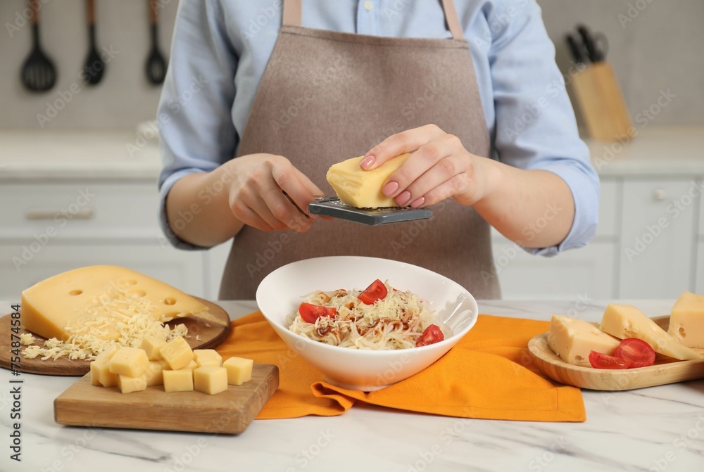 Woman grating cheese onto delicious pasta at white marble table in kitchen, closeup Woman grating cheese onto delicious pasta at white marble table in kitchen, closeup