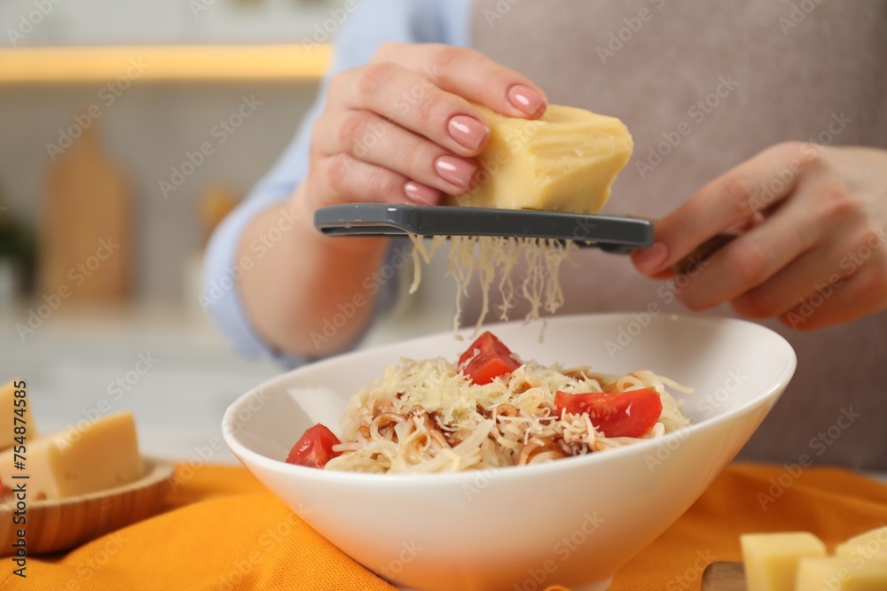 Woman grating cheese onto delicious pasta at table in kitchen, closeup Woman grating cheese onto delicious pasta at table in kitchen, closeup