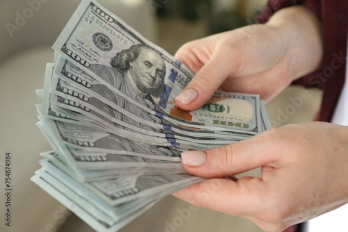 Money exchange. Woman counting dollar banknotes on blurred background, closeup