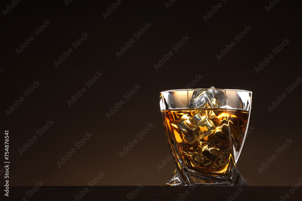 Whiskey with ice cubes in glass on table against brown background. Space for text Whiskey with ice cubes in glass on table against brown background. Space for text