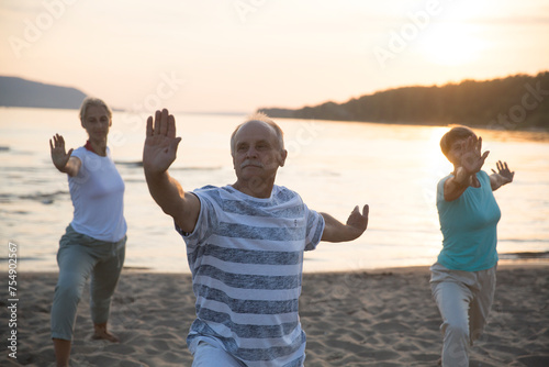 group elderly of people practice Tai Chi Chuan  at sunset on the beach.  Chinese management skill Qi's energy. Healthy lifestyle  photo