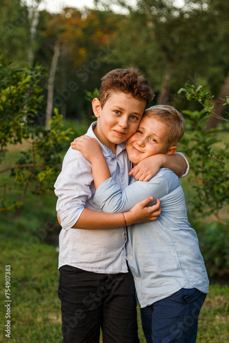 Two cute brothers hugging, dressed in shirts, posing in the park. Vertical view. © Corina