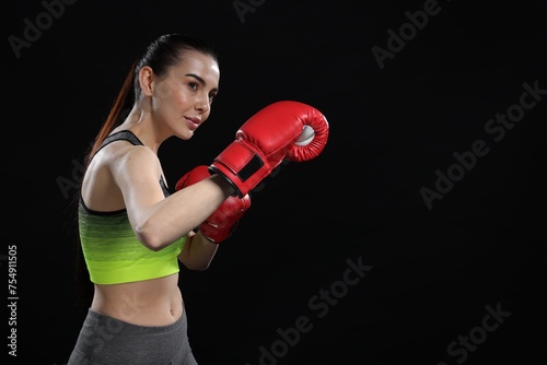 Beautiful woman in boxing gloves training on black background. Space for text © New Africa