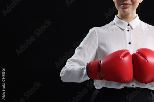 Businesswoman in shirt wearing boxing gloves on black background, closeup. Space for text © New Africa