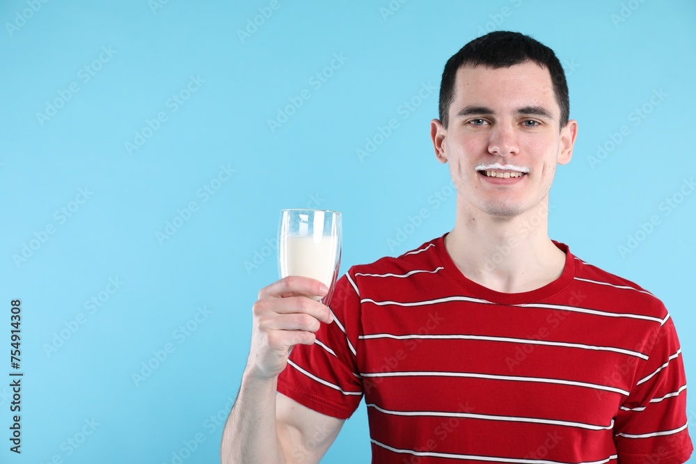 Happy man with milk mustache holding glass of tasty dairy drink on light blue background, space for text Happy man with milk mustache holding glass of tasty dairy drink on light blue background, space for text