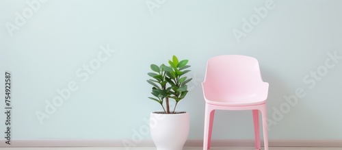 A pink plastic chair is positioned next to a potted plant in a minimalist style setting. The chair adds a pop of color against the green foliage of the plant.