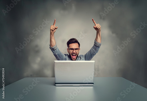 A man sitting with laptop, his hands raised happily