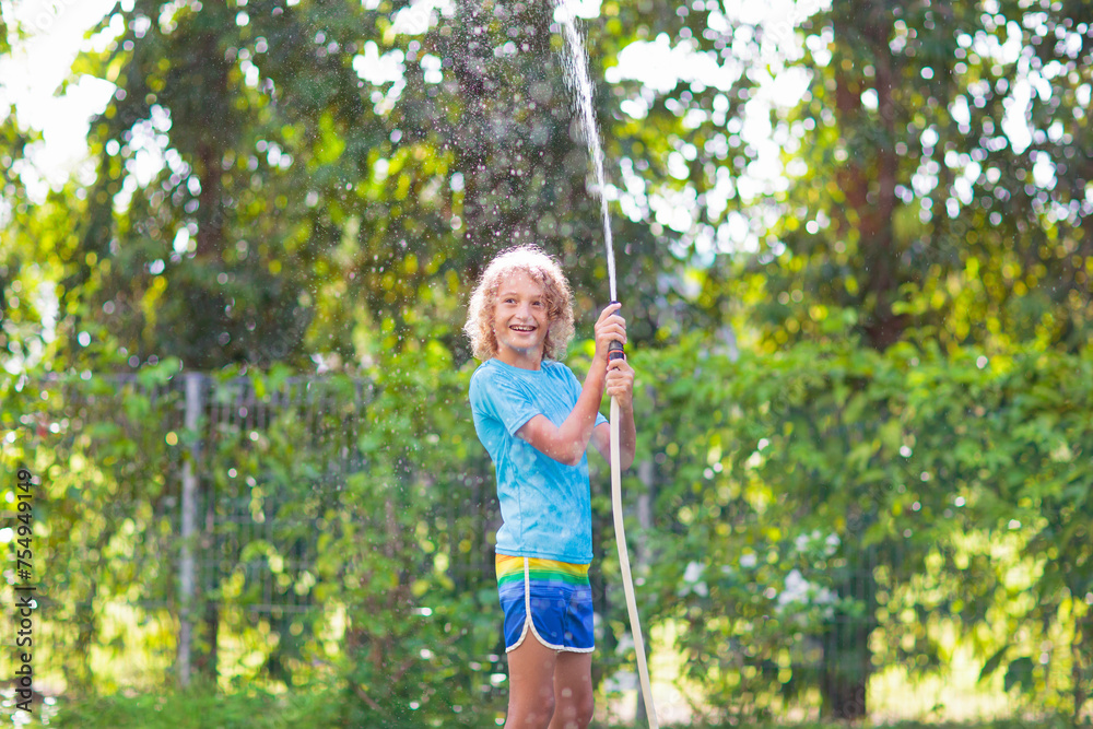 Kids play with water sprinkle hose. Summer garden