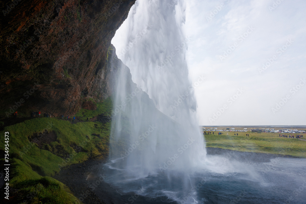 Seljalandsfoss, a famous and unique waterfall in Iceland with visitors walking behind the falls into a small cave. Trip concept.
