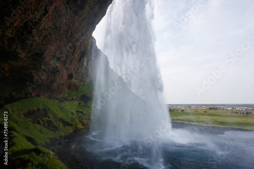 Seljalandsfoss, a famous and unique waterfall in Iceland with visitors walking behind the falls into a small cave. Trip concept.