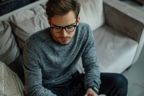Multitasking. Handsome young man wearing glasses and working with touchpad while sitting on the couch 